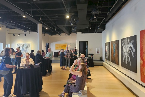 People at an art gallery with abstract paintings on the walls, engaging in conversation and observing the art displayed.