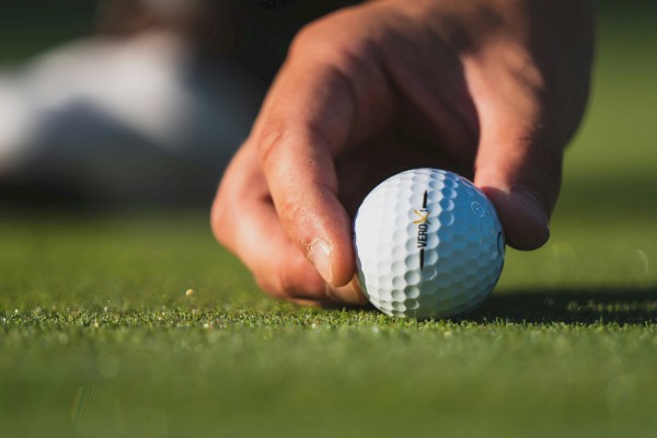 A hand is placing a golf ball on the green of a golf course, preparing for a shot in the game.