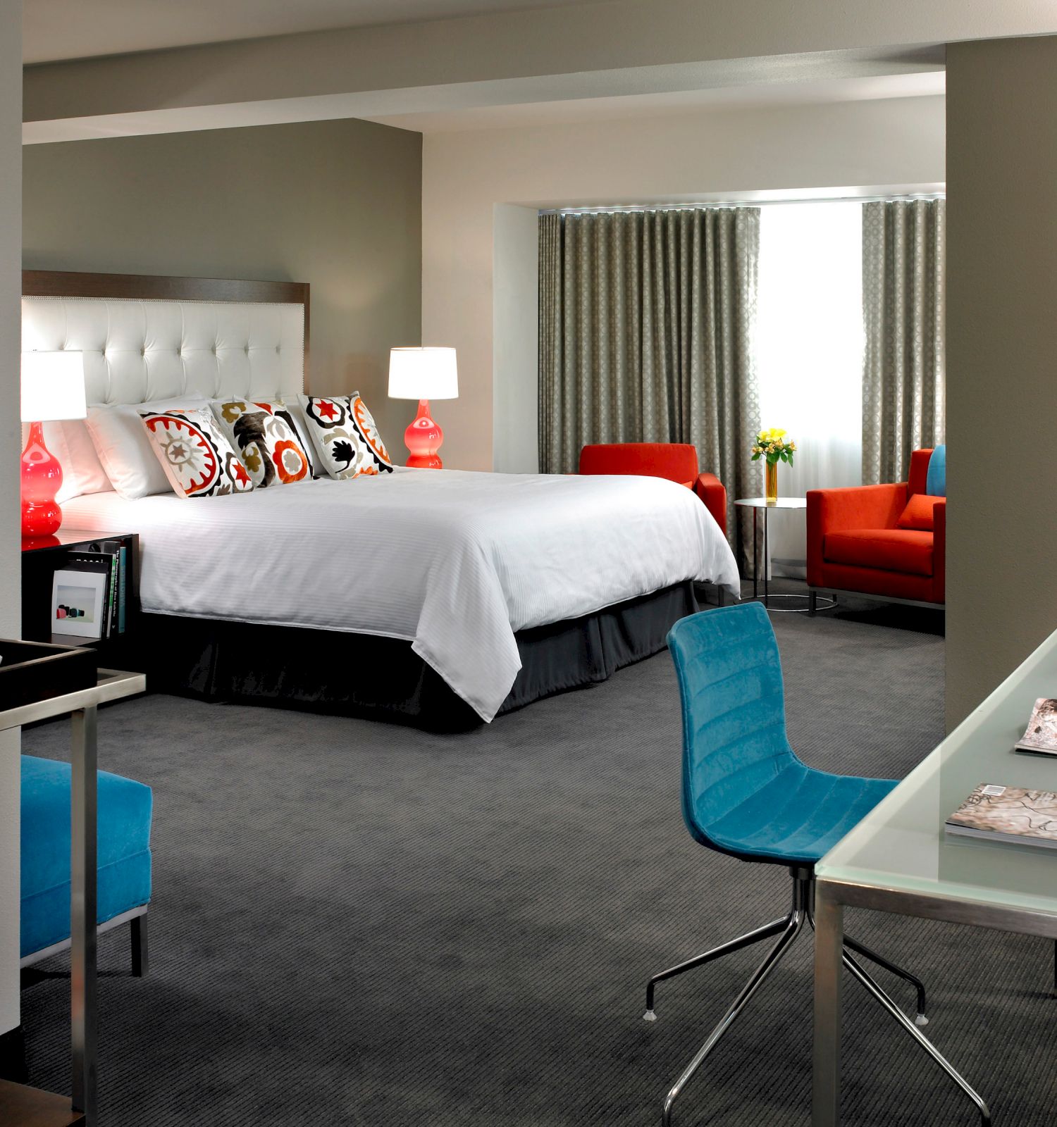 A modern hotel room with a bed, workspace with a blue chair, and seating area. It's well-lit with contemporary decor and amenities.