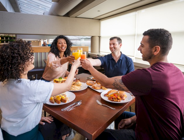 Four people are sitting at a dining table, raising their glasses in a toast, with various dishes on the table.