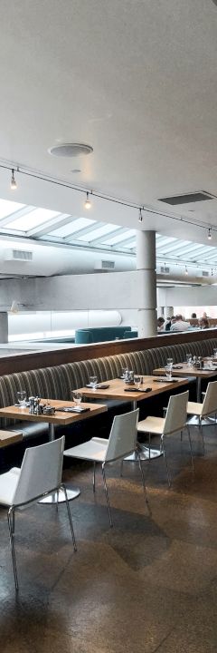 The image shows a modern dining area with tables, chairs, and skylights above, providing ample natural light. The space looks clean and organized.