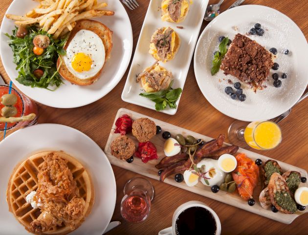 The image shows a table set with various breakfast dishes, including waffles, eggs, salad, pastries, and drinks.