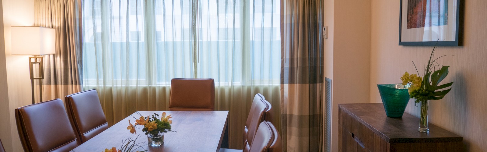 A conference room with a long table, chairs, floral arrangements, a modern chandelier, and framed artwork on the wall.