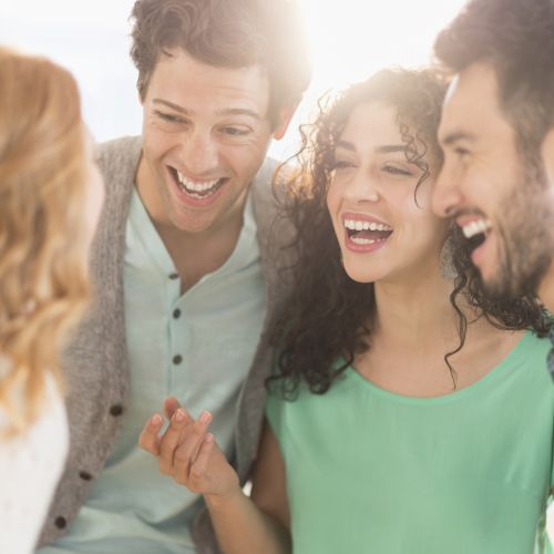 Four people are gathered together, smiling and laughing, with a bright light in the background, creating a warm and cheerful atmosphere.