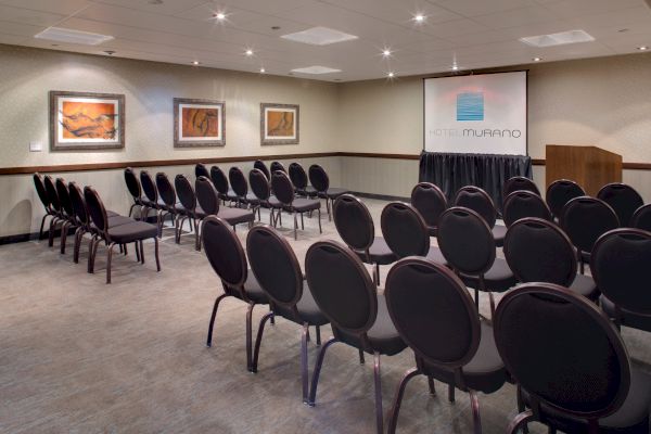 A conference room with rows of black chairs facing a screen and podium, decorated with framed artwork on the walls.