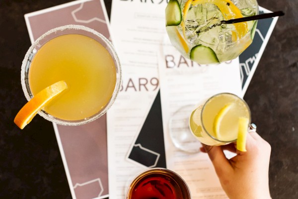 Four drinks on a table with a person's hand holding one, along with bar menus labeled 