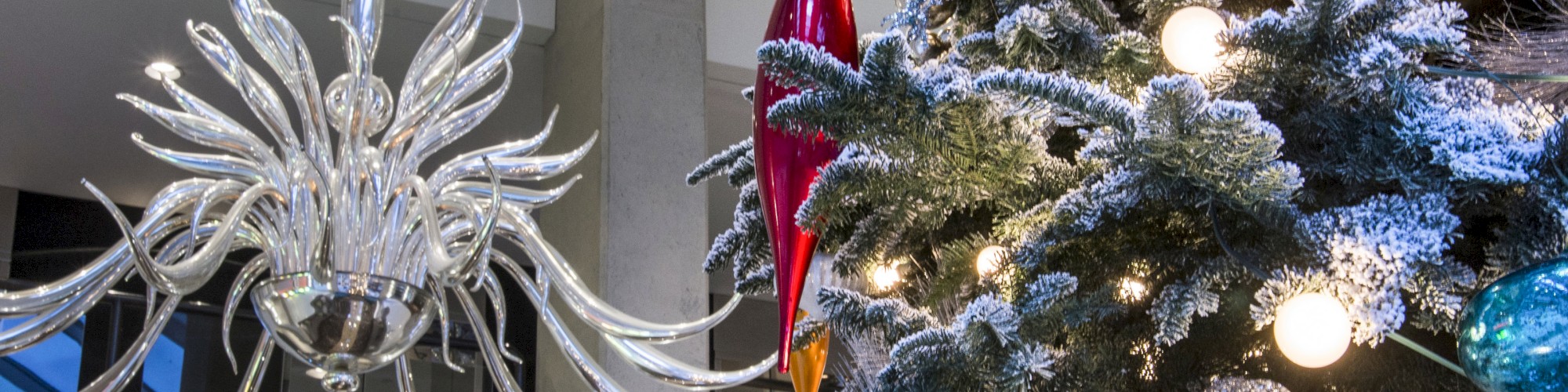 A decorated Christmas tree adorned with lights and ornaments stands next to an intricate chandelier in an indoor setting.