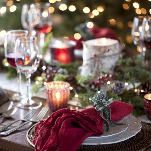 A festive table setting with lit candles, wine glasses, and elegant napkins decorated with greenery, creating a warm and inviting atmosphere.