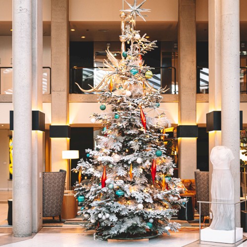 The image shows a large, elaborately decorated Christmas tree in the center of a spacious indoor area, likely within a shopping mall or hotel lobby.