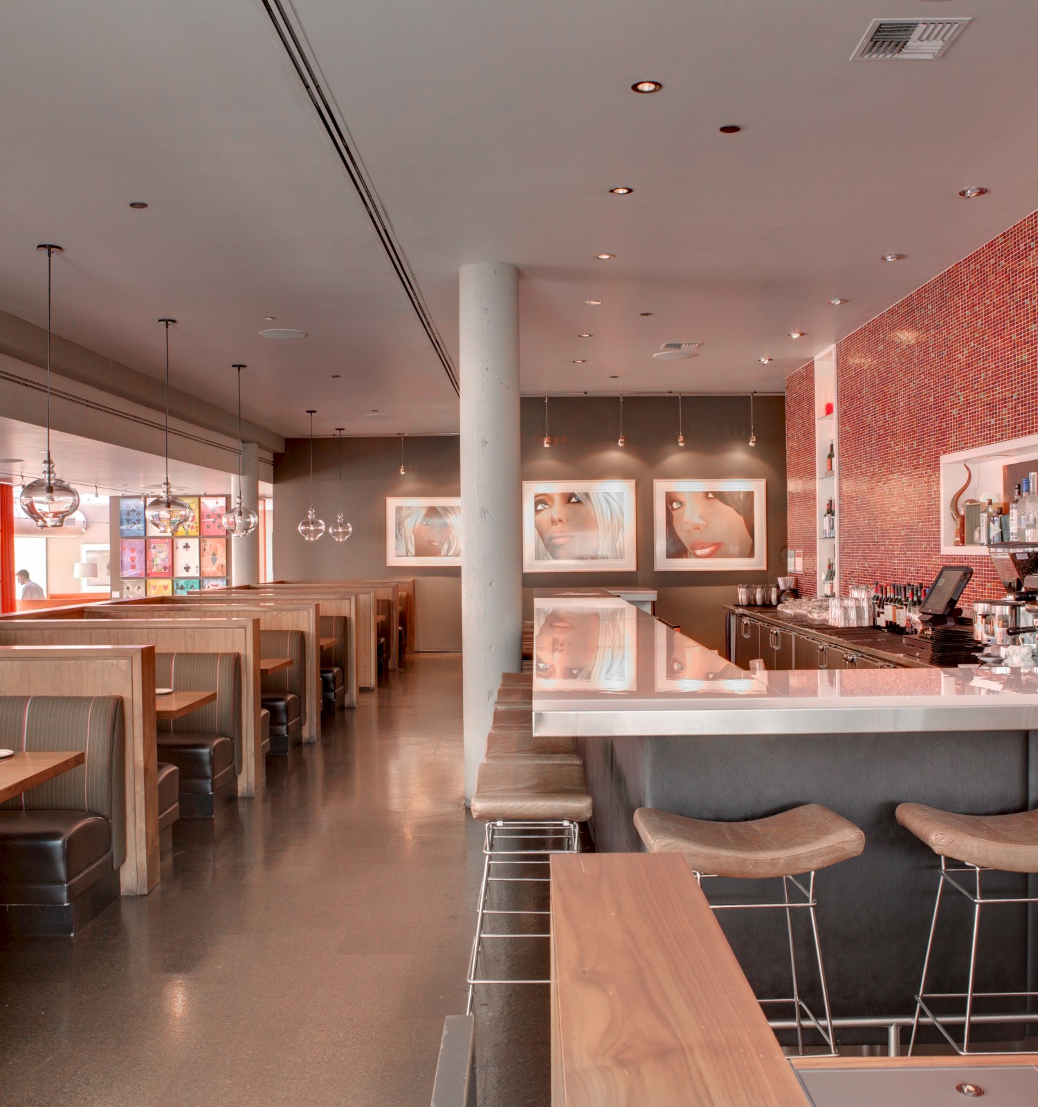 The image shows a modern restaurant interior with booth seating on the left and a bar with high stools on the right, featuring red tile accents.