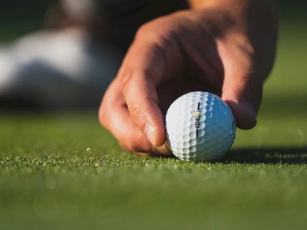 A hand is placing a golf ball on the grass, with a blurred background.