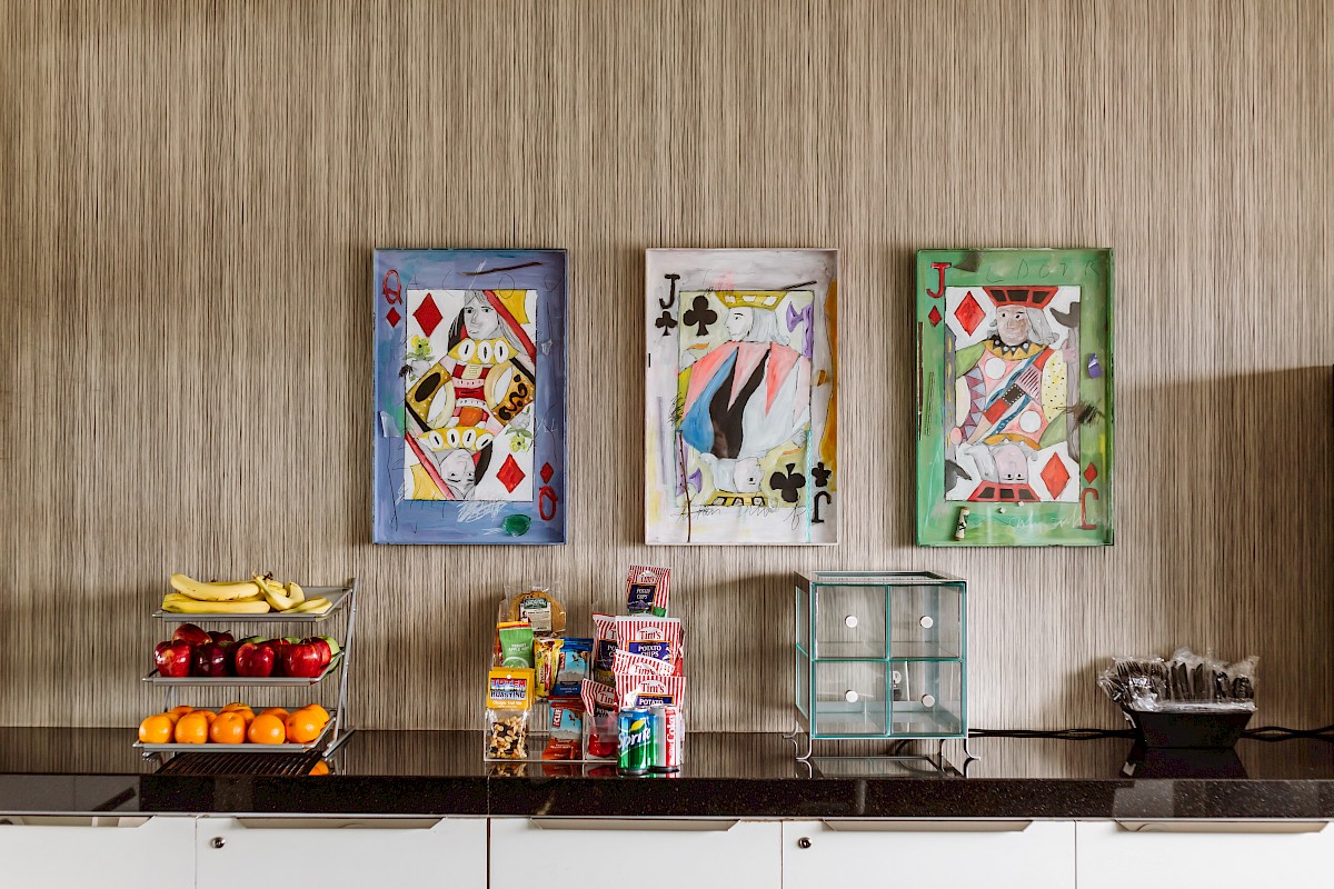 The image shows a countertop with fruit, snacks, and three colorful framed art pieces featuring playing card designs on the wall.