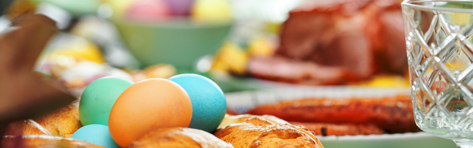 A festive table with colorful eggs, braided bread, and a glass, indicating an Easter or spring celebration.