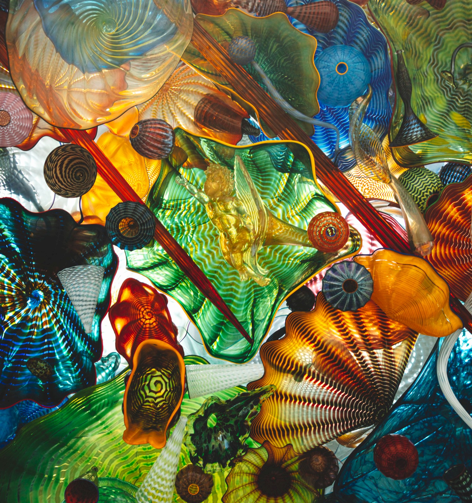 The image shows an intricate arrangement of colorful, abstract glass shapes overlapping, creating a vibrant, artistic composition.